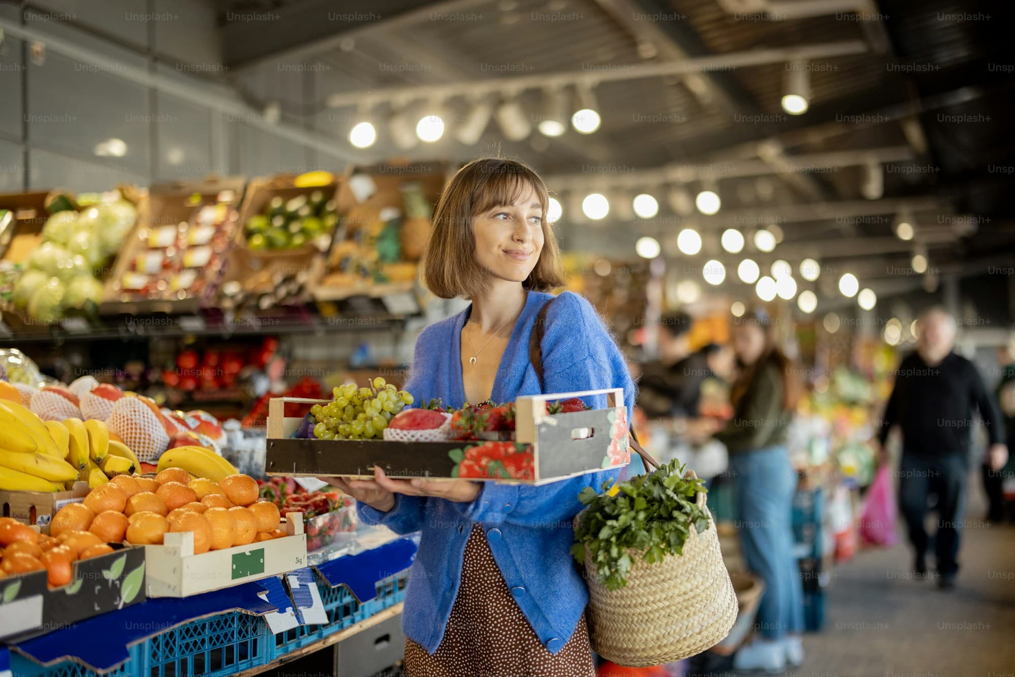 A smiling woman holding a box of fresh fruit and berries at a local market